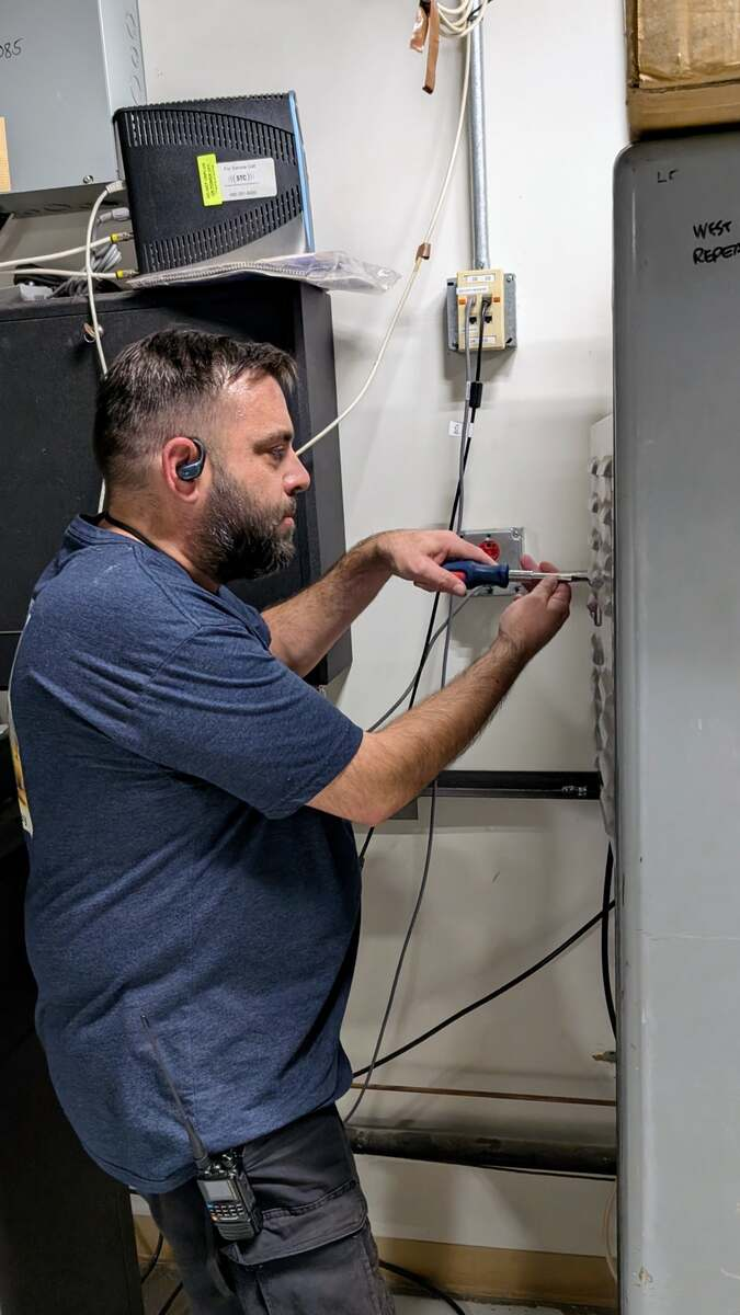 Josh Cavender, KE7WIL, checking connections beside the NY7S repeater rack in the elevator machine room.
