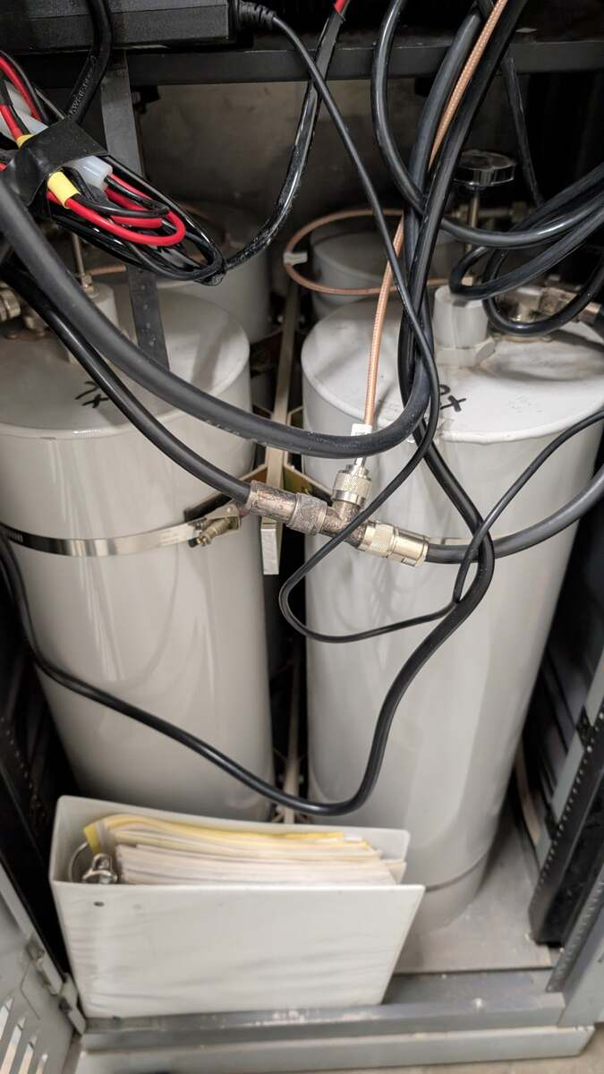 Large white cylindrical cavity duplexers installed behind the NY7S repeater rack, with transmit and receive coax connections visible.